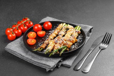 Kızarmış kuşkonmaz, üzerine parmesan peyniri serpiştirilmiş ve siyah arka planda taze vişneli domatesle servis edilmiş domuz pastırması. Gurme yemek, yemek tarifi, mutfak veya restoran menüsü