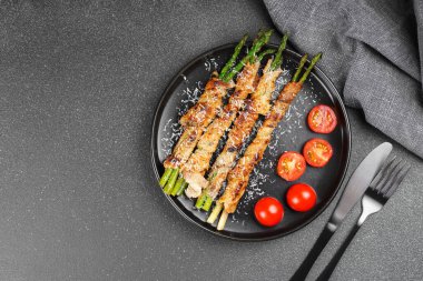 Taze vişneli domatesle servis edilen kuşkonmaz sarılmış lezzetli domuz pastırması ve gri arka plan. Üst görünüm, boşluğu kopyala. Mutfak blogu, menü veya sağlıklı yemek promosyonu için yiyecek arkaplanı.