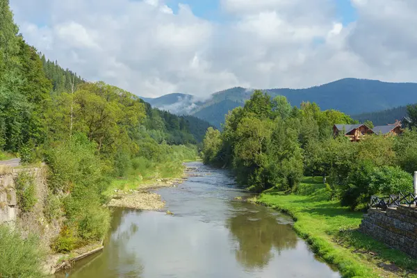 Karpat Dağları 'ndaki yemyeşil orman boyunca uzanan güzel nehir bulutlu mavi bir gökyüzünün altında. Seyahat ve doğa fotoğrafçılığı için ideal bir ortam..