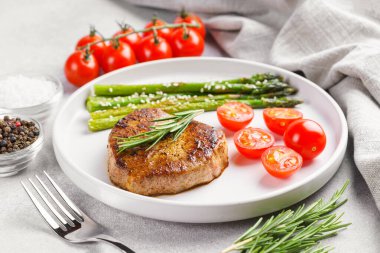 Yakından bakınca, yeşil kuşkonmaz ve beyaz tabakta, çatal bıçakla servis edilmiş vişneli domatesle servis edilen lezzetli biftek makrosu. Yemek menüsü, diyet ya da mutfak tasarımı için mükemmel..