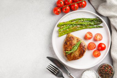 Lezzetli ızgara biftek, yeşil kuşkonmaz ve beyaz tabakta vişneli domates, çatal bıçak ve baharatla servis ediliyor. Yemek menüsü, diyet ya da mutfak tasarımı için mükemmel. Üst görünüm, alanı kopyala