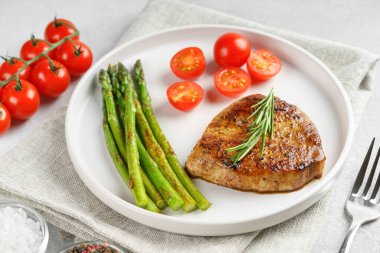 Yakından bakınca, yeşil kuşkonmaz ve beyaz tabakta, çatal bıçakla servis edilmiş vişneli domatesle servis edilen lezzetli biftek makrosu. Yemek menüsü, diyet ya da mutfak tasarımı için mükemmel..