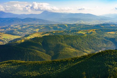 Yeşil kozalaklı orman ve vadilerle kaplı çoklu dağ sırtlarının atmosferik görüntüsü bulutlu gökyüzünün altında kayboluyor. Yaz sisi ve yumuşak güneş ışığı huzurlu ve görkemli bir manzara yaratır..