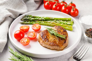 Yakından bakınca, yeşil kuşkonmaz ve beyaz tabakta, çatal bıçakla servis edilmiş vişneli domatesle servis edilen lezzetli biftek makrosu. Yemek menüsü, diyet ya da mutfak tasarımı için mükemmel..