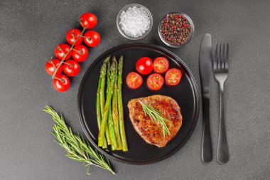 Taze vişneli domatesle servis edilen kuşkonmaz sarılmış lezzetli domuz pastırması ve gri arka plan. Üst manzara, düz yatış. Mutfak blogu, menü veya sağlıklı yemek promosyonu için yiyecek arkaplanı.