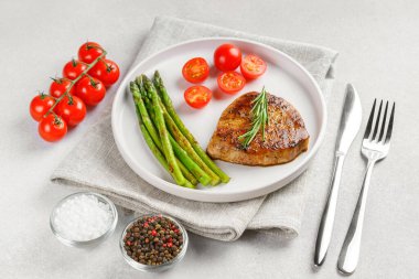 Yakından bakınca, yeşil kuşkonmaz ve beyaz tabakta, çatal bıçakla servis edilmiş vişneli domatesle servis edilen lezzetli biftek makrosu. Yemek menüsü, diyet ya da mutfak tasarımı için mükemmel..