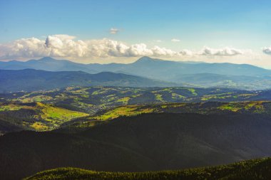 Yeşil kozalaklı orman ve vadilerle kaplı çoklu dağ sırtlarının atmosferik görüntüsü bulutlu gökyüzünün altında kayboluyor. Yaz sisi ve yumuşak güneş ışığı huzurlu ve görkemli bir manzara yaratır..