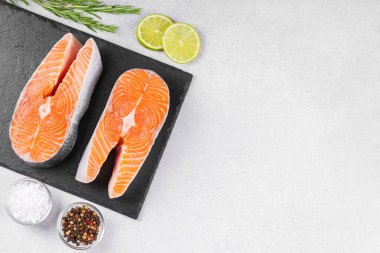 İki taze çiğ somon bifteği ve besin maddeleri. Domates, limon, biberiye, tuz ve biber. Sağlıklı beslenme, deniz ürünleri, yemek pişirme, tarif ve menü kavramları. Üst görünüm, alanı kopyala