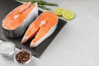 İki taze çiğ somon bifteği ve besin maddeleri. Domates, limon, biberiye, tuz ve biber. Sağlıklı beslenme, deniz ürünleri, yemek pişirme, tarif ve menü kavramları. Üst görünüm, alanı kopyala