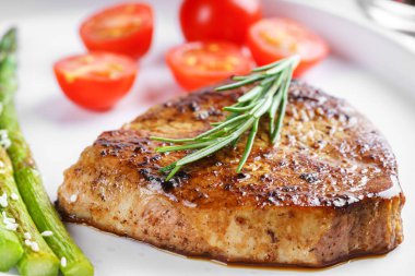 Yakından bakınca, yeşil kuşkonmaz ve beyaz tabakta, çatal bıçakla servis edilmiş vişneli domatesle servis edilen lezzetli biftek makrosu. Yemek menüsü, diyet ya da mutfak tasarımı için mükemmel..