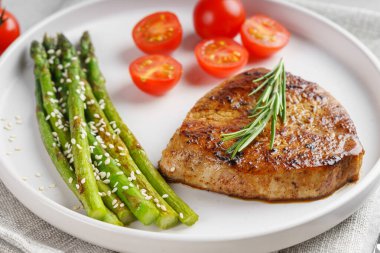 Yakından bakınca, yeşil kuşkonmaz ve beyaz tabakta, çatal bıçakla servis edilmiş vişneli domatesle servis edilen lezzetli biftek makrosu. Yemek menüsü, diyet ya da mutfak tasarımı için mükemmel..