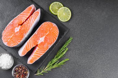 İki taze çiğ somon ya da besin maddeleri içeren siyah taş yüzeyde alabalık bifteği. Domates, limon, biberiye, tuz ve biber. Sağlıklı beslenme, deniz ürünleri, yemek pişirme, yemek tarifi ve menü. Üst görünüm, alanı kopyala