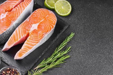 İki taze çiğ somon ya da besin maddeleri içeren siyah taş yüzeyde alabalık bifteği. Domates, limon, biberiye, tuz ve biber. Sağlıklı beslenme, deniz ürünleri, yemek pişirme, yemek tarifi ve menü. Üst görünüm, alanı kopyala