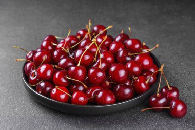 Koyu gri desenli arka plana yerleştirilmiş olgun kırmızı kirazla dolu siyah tabağı kapat. Lezzetli yemekler, sulu yaz meyveleri ve sağlıklı yiyecekler..