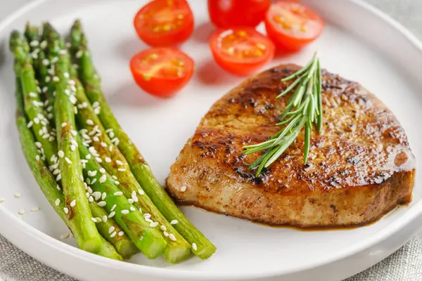 Yakından bakınca, yeşil kuşkonmaz ve beyaz tabakta, çatal bıçakla servis edilmiş vişneli domatesle servis edilen lezzetli biftek makrosu. Yemek menüsü, diyet ya da mutfak tasarımı için mükemmel..