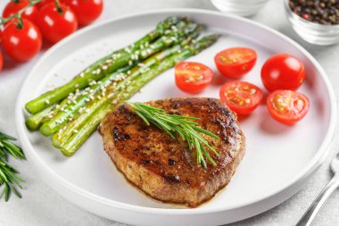 Yakından bakınca, yeşil kuşkonmaz ve beyaz tabakta, çatal bıçakla servis edilmiş vişneli domatesle servis edilen lezzetli biftek makrosu. Yemek menüsü, diyet ya da mutfak tasarımı için mükemmel..