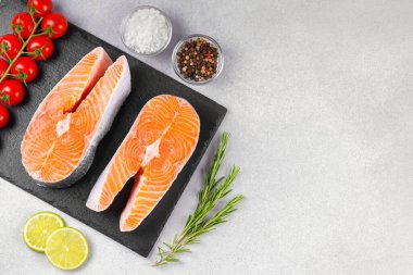 İki taze çiğ somon bifteği ve besin maddeleri. Domates, limon, biberiye, tuz ve biber. Sağlıklı beslenme, deniz ürünleri, yemek pişirme, tarif ve menü kavramları. Üst görünüm, alanı kopyala