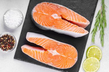 İki taze çiğ somon ya da besin maddeleri içeren beyaz taş yüzeyde alabalık bifteği. Domates, limon, biberiye, tuz ve biber. Sağlıklı beslenme, deniz ürünleri, yemek pişirme, tarif ve menü kavramları.