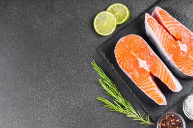 İki taze çiğ somon ya da besin maddeleri içeren siyah taş yüzeyde alabalık bifteği. Domates, limon, biberiye, tuz ve biber. Sağlıklı beslenme, deniz ürünleri, yemek pişirme, yemek tarifi ve menü. Üst görünüm, alanı kopyala