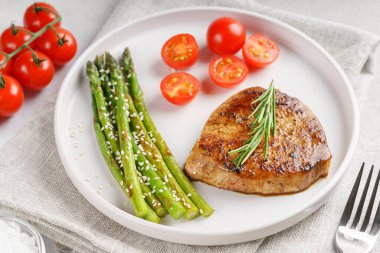 Yakından bakınca, yeşil kuşkonmaz ve beyaz tabakta, çatal bıçakla servis edilmiş vişneli domatesle servis edilen lezzetli biftek makrosu. Yemek menüsü, diyet ya da mutfak tasarımı için mükemmel..