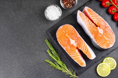 İki taze çiğ somon ya da besin maddeleri içeren siyah taş yüzeyde alabalık bifteği. Domates, limon, biberiye, tuz ve biber. Sağlıklı beslenme, deniz ürünleri, yemek pişirme, yemek tarifi ve menü. Üst görünüm, alanı kopyala