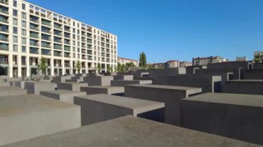 Güneşli bir günde Berlin 'deki Soykırım Anıtı' nın beton yapısına geniş bir bakış açısı ve açık bir gökyüzü. Kameranın solunda yavaş hareket