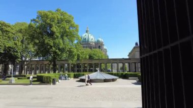 Berlin, Mayıs 2023 - Berlin Müzesi Adası 'ndaki bir bahçe meydanında kamera hareketleriyle yürüyün. Arka planda uzun bir verandanın kemerleri ve güneşli bir günde açık gökyüzü olan bir katedralin kubbesi.