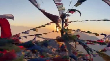 Birçok Tibet Budist duası Himalaya dağlarının zirvesinde güçlü bir rüzgarda dalgalanan bayraklar. Arkaplanda güneş, aralığın arkasında yükseliş.