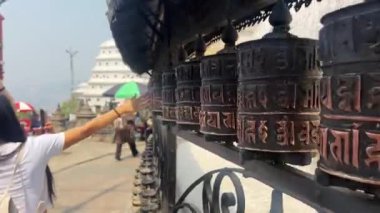 Nepal, Nisan, 2024 - Bir tapınak merkezinde geleneksel Budist ve Tibet dua tekerlerini döndüren turist bir kızın arkasından görünüm