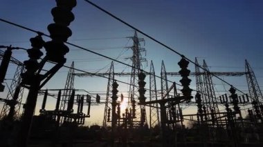 Elektrik parçalarının siluetleri ve gün batımında bir elektrik santralinin yapısal elementleri. Güneş, kameranın hareketi nedeniyle binanın içinde belirir ve kaybolur..