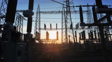Elektrik parçalarının siluetleri ve gün batımında bir enerji santralinin yapısal elementleri. Güneş, kameranın hareketi nedeniyle binanın içinde belirir ve kaybolur..