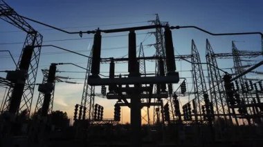 Elektrik parçalarının siluetleri ve gün batımında bir enerji santralinin yapısal elementleri. Güneş, kameranın hareketi nedeniyle binanın içinde belirir ve kaybolur..