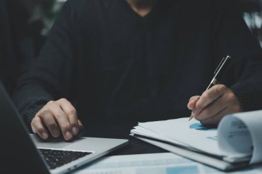 İş adamı ellerinin kalem tutuşu pazarlama grafiği planına finansal yatırım ve iş stratejisi veri tablosu raporuna işaret ediyor ve ofiste dizüstü bilgisayar üzerinde çalışıyor.
