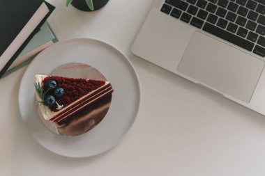 Beyaz arka planda parlak bir dizüstü bilgisayarın yanında nefis bir pastanın üst görüntüsü.