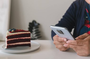 Kafede cep telefonu ve kek tutan ve kullanan bir kadın..