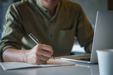 Masada dizüstü bilgisayarla notlar yazan bir adam. Çevrimiçi eğitim ve eğitim alanında dijital ve teknolojinin ilham ve motivasyon kavramını bulması