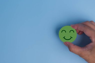 Müşteri hizmetleri değerlendirmesi ve memnuniyet araştırması konsepti. Mavi arka planda ahşap küpte el ele tutuşan mutlu gülümseme yüz ikonu. Boşluğu kopyala