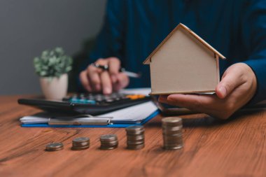 Hesap makinesine basmak, model bir ev tutmak ve masaya bozuk para istiflemek..