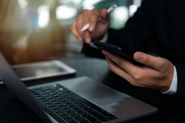 Ofiste dizüstü bilgisayarı olan bir masada cep telefonu tutan bir iş adamı.