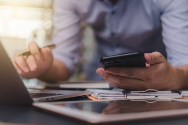 Businessman hand holding mobile smartphone on a table with a laptop at office...	