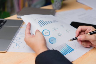 İş belgesi veri performans analizleri ve istatistiksel raporların basılması ve masa başında pazarlama ve mali strateji planlama konularının değerlendirildiği profesyonel bir elin yakın plan çekimi.