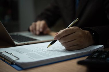 Bir adam bir kağıt parçasına kalemle yazıyor. Takım elbise ve kravat takıyor.