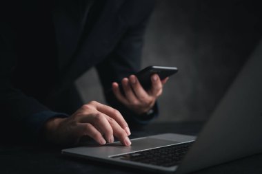 Bilgisayarda yazarken akıllı telefon kullanan bir kişi. Modern internet iletişimini temsil ediyor