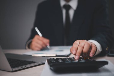 Masada çalışan takım elbiseli bir iş adamının yakın çekimi. Hesap makinesi, dökümanları analiz. Profesyonel, finansal hesaplamalara odaklanmış. İş ve finans için uygun,