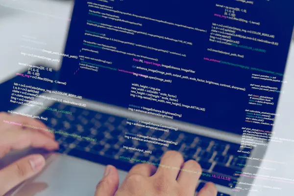 Dizüstü bilgisayarda yazı yazan eller, iş yerinde bir yazılım geliştiricisini gösteriyor. Programlama ve yazılım geliştirme sürecini temsil eder. Teknoloji blogları, kodlama dersleri ve IT eğitim materyalleri için ideal.