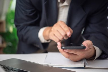 Ofis ortamında akıllı telefon kullanan bir iş adamı dijital finans ve iletişimi temsil ediyor. Fintech hizmetleri ve mobil bankacılık uygulamaları için elverişli
