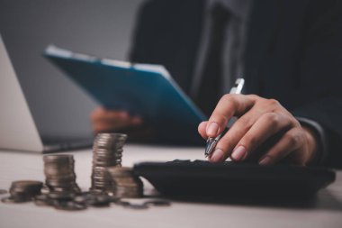 Madeni para yığınları, pano ve hesap makinesiyle mali hesaplar yapan işadamı, mali planlama ve analizi vurguluyor. Mali, muhasebe ve iş hizmetleri için uygundur.