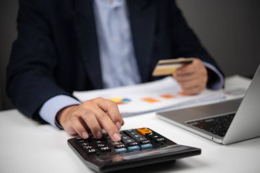İş adamı kredi kartı tutarken hesap makinesi kullanıyor. Mali işlem giderlerini hesaplıyor. Mali yönetim, e-ticaret veya bankacılık için ideal