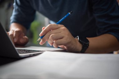 Bilgisayarda yazarken elinde kalem tutan kişi işe odaklanmış. Şirket için uygun, profesyonel.,