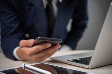 Ofis ortamında akıllı telefon kullanan bir iş adamı dijital finans ve iletişimi temsil ediyor. Fintech hizmetleri ve mobil bankacılık uygulamaları için elverişli